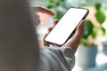 A man is using a smartphone with a blank, frameless screen in a contemporary home or office interior. Bright light with plants in