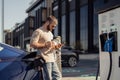 Man using smartphone while charging electric car