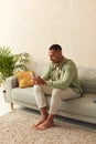 Man Using Smartphone At Home. Handsome Multiracial Guy Sitting On Sofa