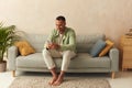 Man Using Smartphone At Home. Handsome Multiracial Guy Sitting On Sofa