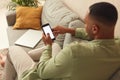 Man Using Smartphone At Home. Handsome Multiracial Guy Sitting On Sofa