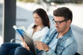 man using tablet and woman reading book at bus-stop Royalty Free Stock Photo