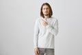 Man is very upset seeing sad commercial. Portrait of gloomy handsome guy with beard in casual white pullover pointing at Royalty Free Stock Photo