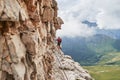 Man on via ferrata Cesare Piazzetta, Dolomites mountains, Italy, close to the rock wall, with a winding road below, in Summer Royalty Free Stock Photo