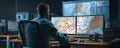Man viewing multiple large map displays on dual monitors in dim control room, focused and analyzing route networks with Royalty Free Stock Photo