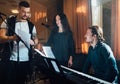 A man in a vocal lesson to accompaniment of piano shows a piece of text with song to a teacher