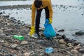 Man volunteer picking up plastic trash on stone beach. Male collecting used plastic bottles in trash bag. Earth Day Royalty Free Stock Photo