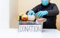 Man volunteer in protective medical mask and gloves puts products in donation box