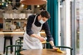 Man waiter wearing mask disinfecting table in the cafe