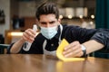 Man waiter wearing mask disinfecting table in the cafe