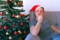 Man is waking up sitting on couch at home near Christmas tree at eve, hangover.
