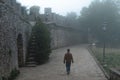 Man walking alone at distance. Fortification on top of the mountain, old castle. Journey. Mystical atmosphere, fog, white haze,