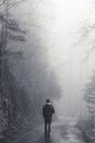 Man walking alone on a road through a dark foggy forest Royalty Free Stock Photo