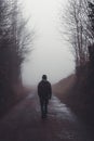 Man walking alone on a road through a dark foggy forest Royalty Free Stock Photo