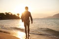 Man, walking on beach and ocean with sunset, lens flare with back view and waves on vacation in Hawaii. Tourism, travel Royalty Free Stock Photo