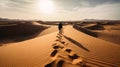 Man walking in the desert with footprints in the sand at sunset.