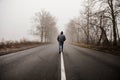 Man walking in a foggy autumn landscape. Lonely man walking in fog. Rural landscape with road in morning mist. Warm autumn colors Royalty Free Stock Photo