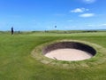 A man walking on a green with a pot bunker on a classic links style course in Brora, Scotland