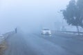 Man walking in heavy fog early morning on roadside with car coming on a road with low visibility Royalty Free Stock Photo