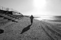 A Man Walking A Long The Beach Towards The Sun On A Cold Winter Morning - In Black And White