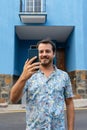 Man walking in the street with his smart phone, making a plan with his college and smiling. Caucasian hipster with beard out of