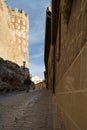 A man walking through a street in Segovia with medieval buildings and a tower with battlements