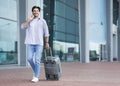 Man Walking With Suitcase Outside Of Airport And Talking On Cellphone