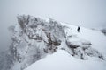 Man walks along the cliff to the top in the snowy misty mountains