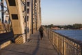 a man walks away across a deserted large automobile bridge over a wide river in the rays of the setting sun