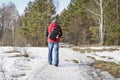 A man walks through the woods in early spring with a photo backpack and trekking sticks