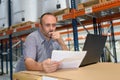 Man in warehouse with laptop looking at papers Royalty Free Stock Photo