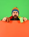 Man in warm hat holds brown and green cups