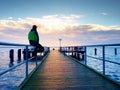 Man in warm jacket and baseball cap sit on pier and enjoy quiet morning sea. Tourist relax.
