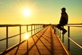 Man in warm jacket and baseball cap sit on pier handrail construction and enjoy morning at sea. Royalty Free Stock Photo