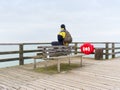 Man in warm jacket and baseball cap sit on wooden pier and enjoy quiet morning sea Royalty Free Stock Photo