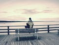 Man in warm jacket and baseball cap sit on wooden pier and enjoy quiet morning sea Royalty Free Stock Photo