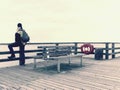 Man in warm jacket and baseball cap sit on wooden pier and enjoy quiet morning sea Royalty Free Stock Photo