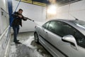 A man washes a car in a box contactless car wash self-service with a water gun in the manual self-service washing