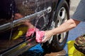 Man washes car wheel. Male hand holds pink sponge with soapy foam for cleaning. Royalty Free Stock Photo
