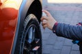 Man after washing applies tire cleaner with a white spray. Orange car at car wash. Male hand and car wheel close up Royalty Free Stock Photo