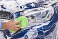 Man washing a soapy blue car with a green sponge