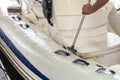 Man washing white inflatable boat with brush and pressure water system at garage. Ship service and seasonal maintenance concept