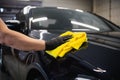 Man after washing wipes black car with a rag at car wash. Male hand and car body close up.