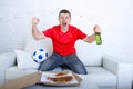 Man watching football game on tv in team jersey celebrating goal crazy happy jumping on sofa Royalty Free Stock Photo