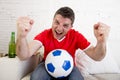 Man watching football on tv wearing team jersey celebrating goal happy on sofa