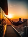 Man watching stunning sunset over the city lying in the hammock. Male relaxing after workday at his big balcony. Generative AI Royalty Free Stock Photo