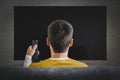 Man watching television, turning on plasma flatscreen TV-set, pointing remote control at empty TV screen on white wall. Guy