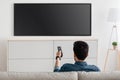 Man watching television, turning on plasma flatscreen TV-set, pointing remote control at empty TV screen on white wall