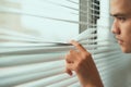 Man watching by the window - young man lowering the window with his fingers to peek - spy on - look through the gap - concept of