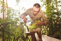 A man is watering plants in a mini-garden in a room, a watering can is made of a plastic bottle